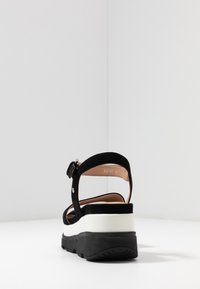 Sandalo nero in suede con cinturino regolabile, suola intermedia bianca e suola esterna nera. Presenta una punta rotonda e un design minimalista.