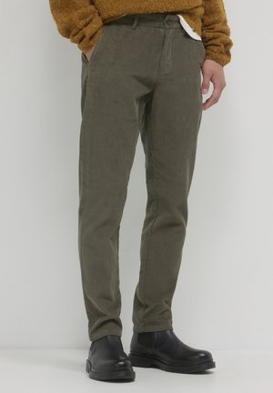 Olive green corduroy trousers with a tapered fit. Features side pockets and a button closure, paired with black ankle boots.