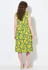 Robe sans manches avec un motif de citrons jaunes et verts, en tissu léger, longueur genoux, dotée de liens décoratifs sur les bretelles.