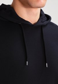 Felpa nera con cappuccio realizzata in tessuto liscio, dotata di coulisse con punte in metallo. Adatta e attillata al collo con un design semplice.