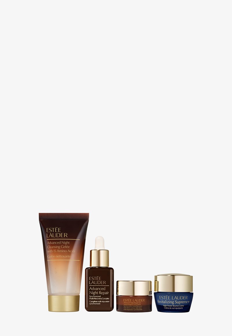 Vier Hautpflegeprodukte: eine braune Tube, eine dunkelbraune Tropferflasche und zwei Tiegel (goldene und blaue Akzente). Alle haben ein elegantes Design.