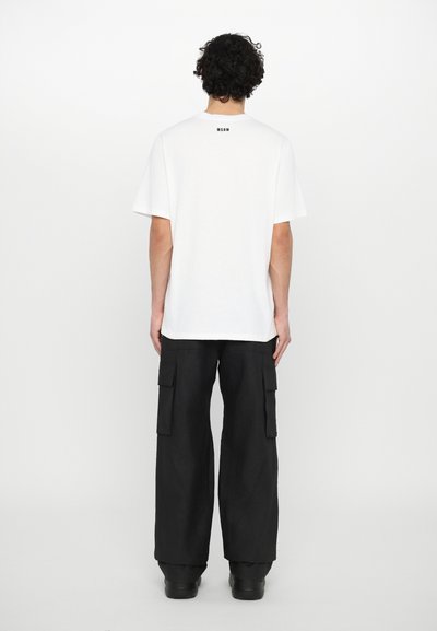 T-shirt bianca in cotone a maniche corte e colletto a girocollo, con un piccolo logo nero sul retro. Abbinata a pantaloni cargo neri.