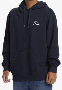 Sudadera con capucha de algodón azul marino con un bolsillo canguro, puños acanalados y un logo de ola bordado en el pecho izquierdo. Tela suave y texturizada.