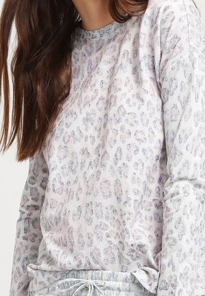 Kobieta ubrane w jasnoszary top z długim rękawem i pasujące spodnie z subtelnym wzorem w panterkę, pokazana częściowo od szyi do bioder.