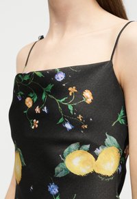 Μαύρο φόρεμα με λεπτές τιράντες, με λουλουδάτο και κίτρινο μοτίβο λεμονιών, φορεμένο από άτομο που δείχνει τον άνω κορμό και το ντεκολτέ.