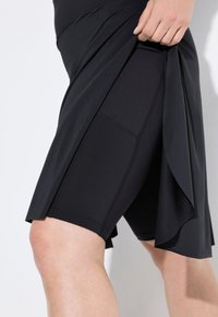 Zwarte sportrok met ingebouwde shorts, met een gelaagd ontwerp en soepel, rekbaar materiaal voor flexibiliteit en comfort.