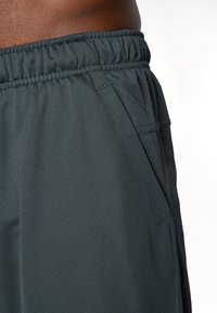 Tumšas pelēkas sporta šortus ar elastīgu jostu, sānu kabatām un teksturētu audumu, kas nodrošina gaisa caurlaidību un komfortu.