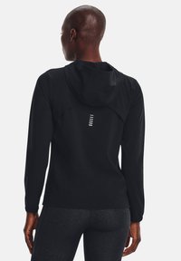 Chaqueta ligera negra con capucha y mangas largas, con un patrón sutil y acentos reflectantes en la espalda.