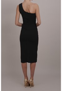 Svart enaxlad klänning med figurnära silhuett, knälång längd, slät tygstruktur och dragkedja bak. Guldklackar kompletterar looken.