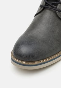 Buty z okrągłym noskiem, z gładką, ciemnoszaro-syntetyczną cholewką, kontrastującymi szwami oraz lekką gumową podeszwą z niebieskim akcentem.