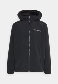 Chaqueta negra con cremallera y capucha, hecha de un tejido ligero. Presenta un logo en el lado izquierdo del pecho y puños elásticos. Diseño simple y sin patrones.