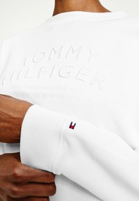 Felpa bianca con logo e indirizzo "TOMMY HILFIGER" a rilievo. Polsini a costine con sottile accento rosso e blu del logo. Tessuto morbido.