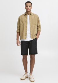 Beige button-up shirt paired with a white t-shirt, black shorts, and white sneakers with beige accents. Casual fit, minimalist design.