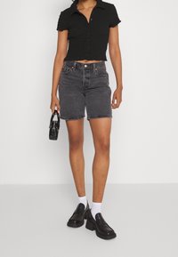 Black textured crop shirt with short sleeves, paired with high-waisted black denim shorts; complemented by black platform shoes and a mini handbag.