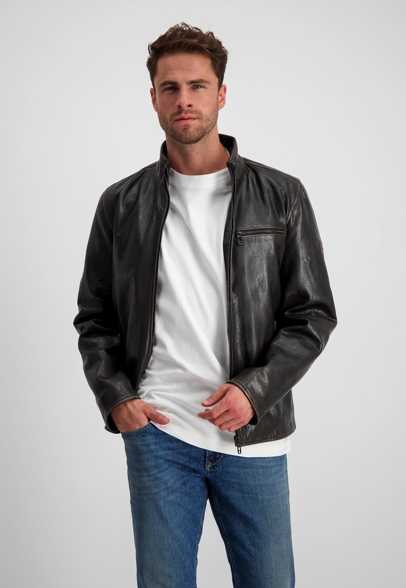 Schwarze Lederjacke mit hohem Kragen, Frontreißverschluss und einer Tasche auf der linken Brust. Das Model trägt ein weißes T-Shirt und Jeans.