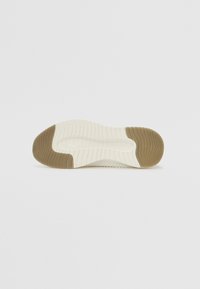White sneaker sole with textured grooves and a brown rubber accent on the underside, featuring a smooth white section near the toe.
