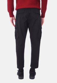 I pantaloni cargo neri presentano una vestibilità comoda con tasche sui lati e sul retro. Abbinati a scarpe nere e a un maglione rosso.