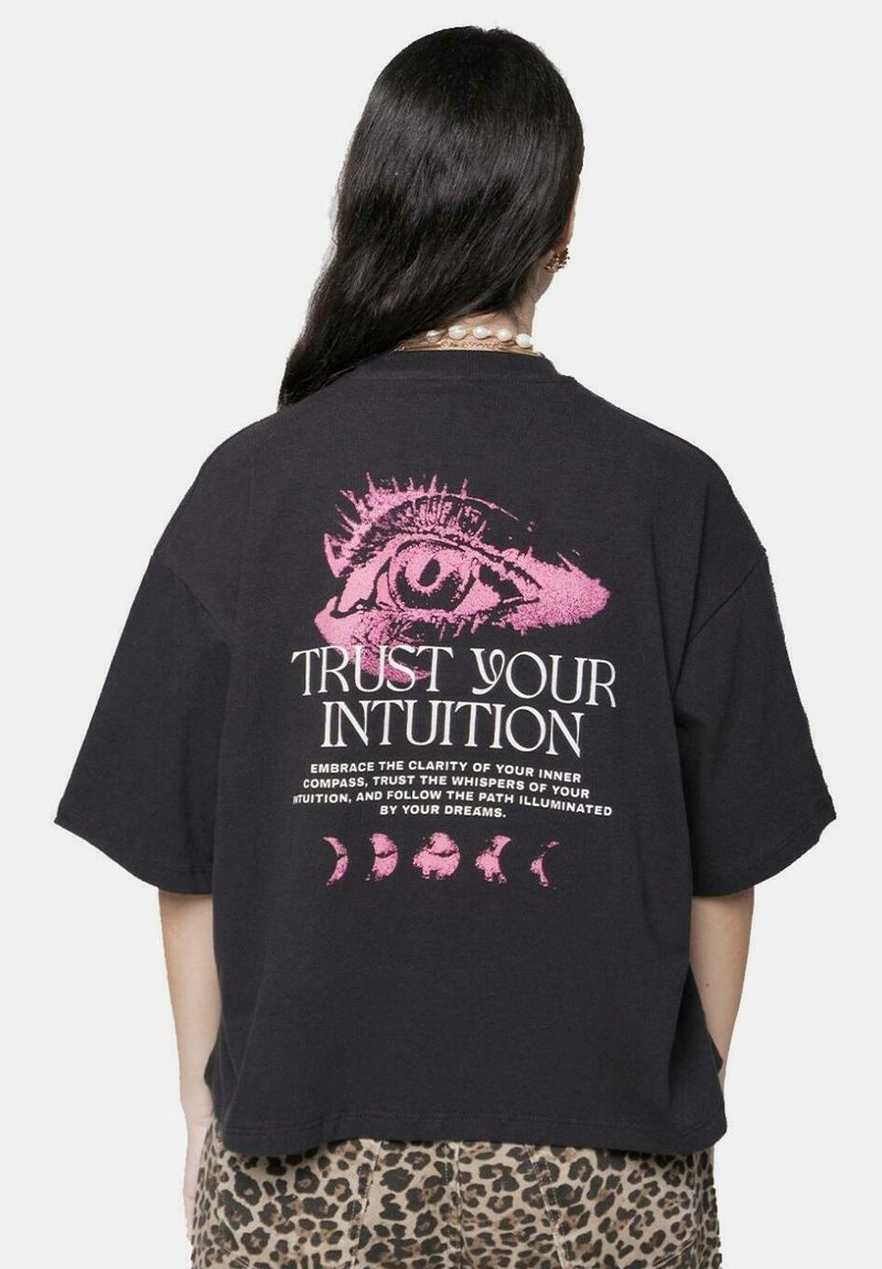 Camiseta negra de gran tamaño con un destacado gráfico de un ojo rosa y el texto "CONFÍA EN TU INTUICIÓN" con fases lunares decorativas debajo.