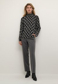 Bluza s uzorkom u crno-bijeloj boji, visokog vrata, dugih rukava; u kombinaciji s sivim hlačama i crnim čizmama na petu do gležnja.