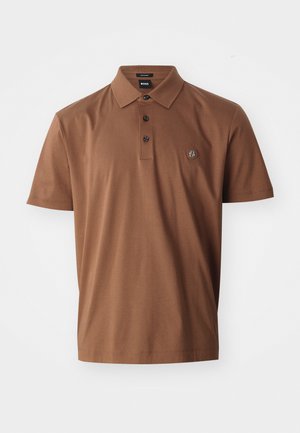 Brun polo-shirt i bomull med en 3-knappsknäppning, korta ärmar och en liten logotyp på vänster bröst. Slät textur.