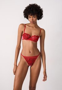 Lace lingerieset in het rood met bloemmotieven. De beha heeft beugels en dunne verstelbare bandjes; de bijpassende string heeft een vergelijkbaar ontwerp.