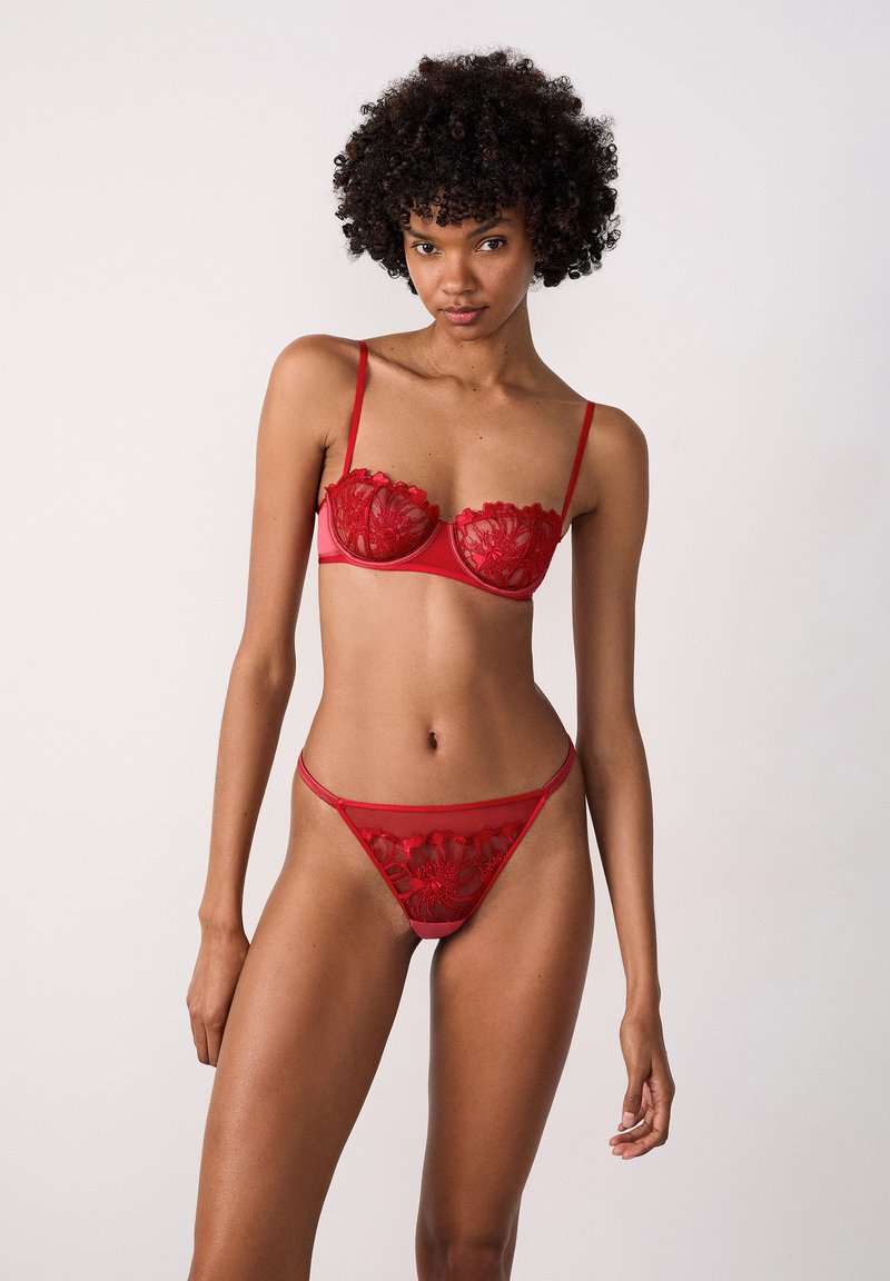 Lace lingerieset in het rood met bloemmotieven. De beha heeft beugels en dunne verstelbare bandjes; de bijpassende string heeft een vergelijkbaar ontwerp.