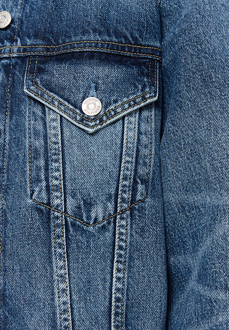 Details einer blauen Jeansjacke, die eine gestickte Brusttasche mit einem silbernen Druckknopf sowie sichtbare Nähte und Textur zeigt.