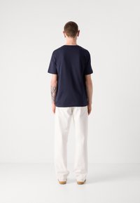 Marineblaues T-Shirt mit kurzen Ärmeln aus Baumwolle, mit einem Rundhalsausschnitt. Kombiniert mit weißen, weit geschnittenen Hosen und braunen Schuhen.
