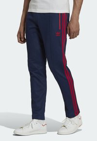 Mörkblå idrottsbyxor med röda sidestreck, avsmalnande design, elastisk midja och broderad logotyp på vänster lår.