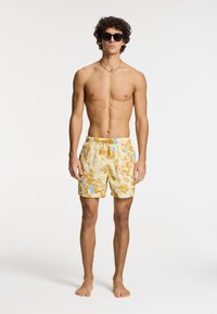 Shorts de bain dans un motif camouflage jaune, bleu et orange, avec une taille élastique et un cordon de serrage. Fabriqués en tissu léger.