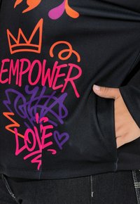 Schwarzer Kapuzenpullover mit buntem, grafischem Text und Designs in Orange, Pink und Lila. Das Design umfasst Kronen- und Herzmotive.