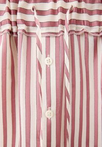 Gros plan d’un tissu rayé verticalement rose et blanc avec des boutons blancs et un détail de couture froncée près du haut.