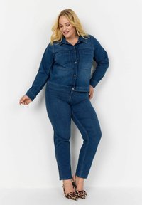 Denim jaka ar pogu priekšpusi un divām krūšu kabatām, apvienota ar denima biksēm. Abas ir tumši zilā toņos. Akcentēta ar leoparda raksta papēžiem.