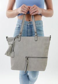 Gray faux leather tote bag with dual straps, front zipper pocket, tassel accent, and polished hardware details. Smooth texture, rectangular shape.