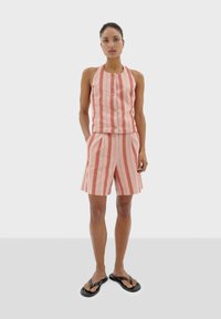 Gestreepte roze en crèmekleurige outfit bestaande uit een haltertop met knopen en bijpassende shorts, gemaakt van lichtgewicht stof, met platte sandalen.