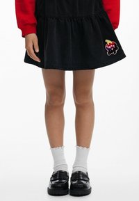 Vestido de mezclilla negro con un dobladillo en capas y un parche colorido de helado. Combinado con calcetas blancas de canalé y mocasines negros.