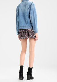 Jeansjacka i ljusblått med en figurnära design, visad över en blommönstrad kjol. Modell som bär svarta klackboots.