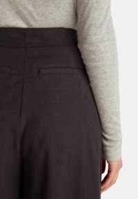 Czarne eleganckie spodnie o gładkiej fakturze, z tylnymi kieszeniami i dopasowaną talią, w połączeniu z szarym longsleeve'em.