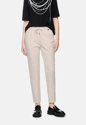 Woman wearing beige drawstring pants, black t-shirt with white necklace print, and black chunky platform loafers against a white background.