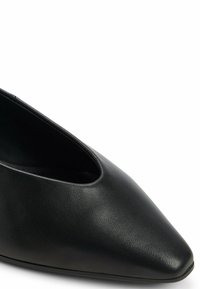 Scarpa in pelle nera con punta affusolata e design a intaglio, caratterizzata da una texture liscia e una silhouette minimalista.
