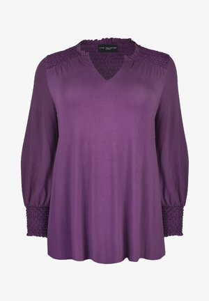 Fioletowa bluzka z dekoltem w serek, marszczonym detalem na ramionach i długimi rękawami. Wykonana z miękkiego materiału z marszczonymi akcentami na mankietach.
