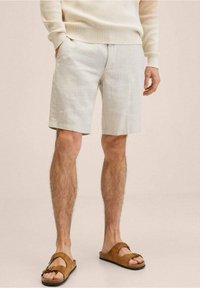 Vaaleanbeige pellavashortsit, muotoiltu malli, edessä taskut. Yhdistetty ruskeisiin sandaaleihin, joissa on kaksi hihnaa ja avonainen varvas.