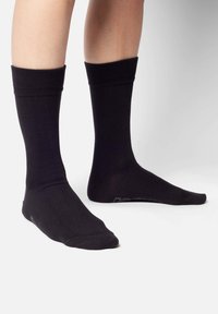 Schwarze Baumwollcrew-Socken mit gerippten Bündchen, glatter Textur und verstärkten Zehen. Mit einem subtilen Branding-Detail nahe dem Knöchel.
