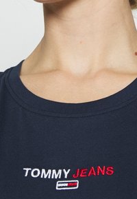 Marinblå ribbad T-shirt med rund halsringning som har broderad "TOMMY JEANS" i vita och röda bokstäver. Slät tygkvalitet.