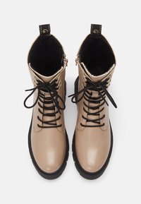 Paire de bottes en cuir beige à lacets avec semelles noires et doublure intérieure noire, vues de dessus sur fond blanc.
