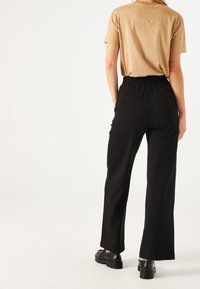 Pantalones de pierna ancha negros con cintura elástica, combinados con una blusa corta de manga corta color beige. Los zapatos son negros con suela gruesa.