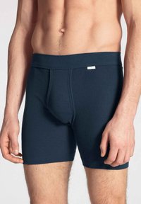Marineblauwe katoenen boxershorts met een gladde textuur, elastische tailleband en een centrale pouch voor ondersteuning, met minimalistische stikseldetails.