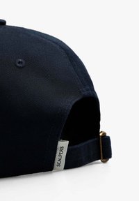 Gorra de béisbol azul marino hecha de tela texturizada, con visera curvada, correa ajustable con un clasp de metal y una etiqueta lateral que dice "SCALPERS."
