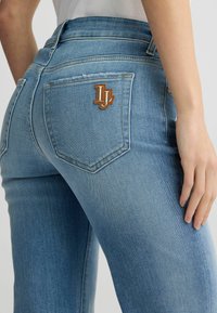 Lichtblauwe denim jeans met een klassiek vijf-pocket ontwerp, een bruine logopatch op de achterzak en zichtbare stikseldetails.