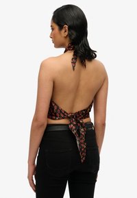Top nero con scollo all'americana e motivo floreale rosso, legato sul retro. Tessuto liscio, design con schiena scoperta, abbinato a jeans neri a vita alta.